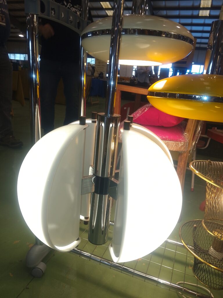 En premier plan, c'est un lustre Spicchio créé par les designers Danilo et Corrado Aroldi pour Stilnovo dans les annéees 70. Il est de couleur blanche et chromé.
En second plan, il y a deux lustres "Space Age" allemands, des annéees 60 : l"un est blanc, l'autre est jaune